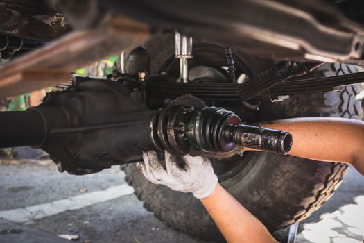 Technician's hand is wearing white cloth gloves, fixing the propulsion shaft of the car.