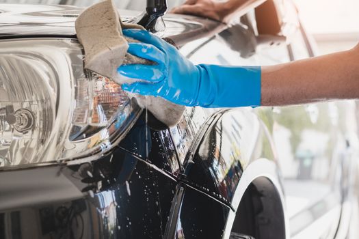 Car wash staff wearing blue rubber gloves using a sponge moistened with soap and water to clean the car.