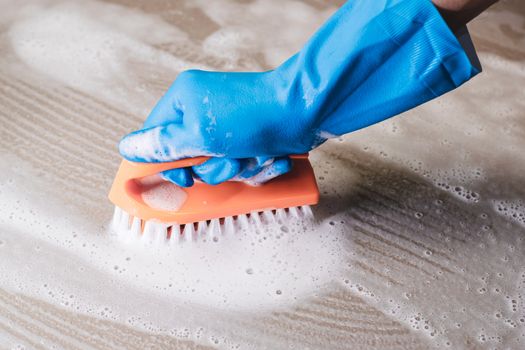 Hand of man wearing blue rubber gloves is used to convert scrub cleaning on the tile floor.