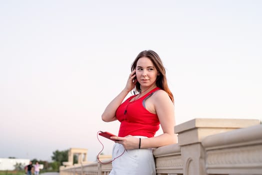 Teenager girl standing in the park listening to the music and chatting on her phone at sunset