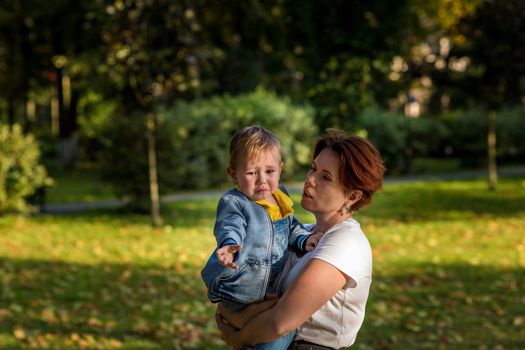 Mom soothes a crying child in her arms in an autumn park at sunset