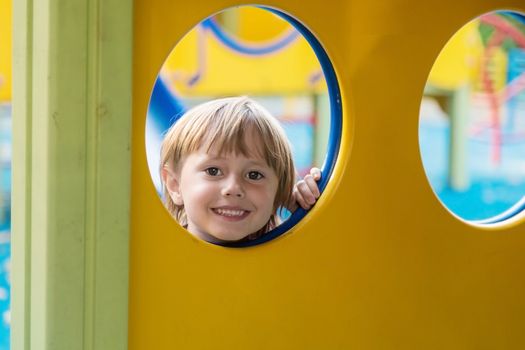 The girl looks out from the circle of the slide on the playground looks at the camera and smiles.