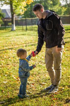 .Dad helps his son in denim to blow bubbles in an autumn park.