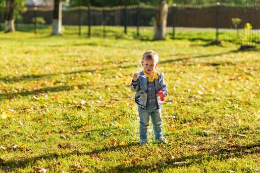 A little boy in denim clothes blows bubbles in the autumn park.