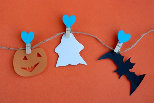 The concept of Halloween. Halloween decorations, pumpkins, bats, ghosts on clothespins with blue hearts on an orange background. Flat bed, top view text space.