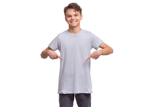 Smiling teen boy, isolated on white background. Happy child pointing fingers at blank t-shirt.