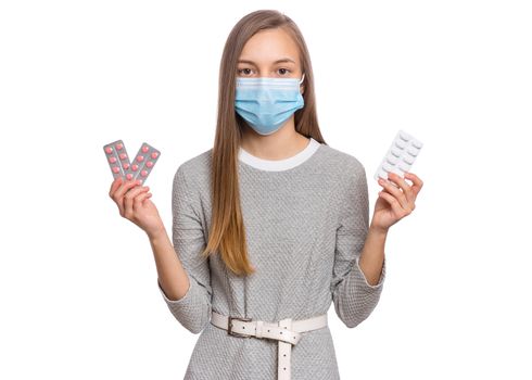 Concept of coronavirus. COVID-19. Child wearing medical face mask - protection from influenza virus, on white background. Teen girl holds pills.
