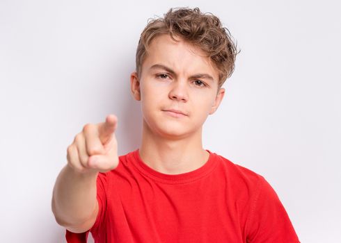 Portrait of happy teen boy pointing finger at camera, front view. Cute serious child in choose you, on gray background. Child in red t-shirt.