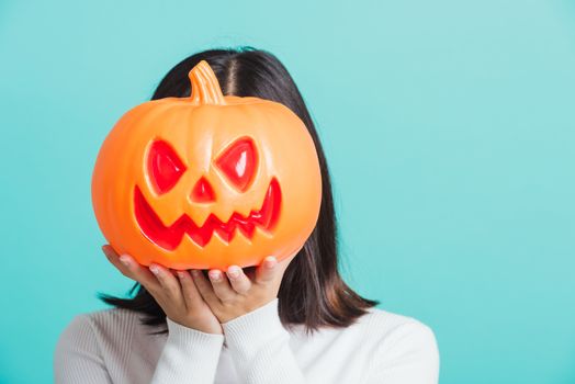 Portrait of Asian beautiful young woman holding orange model pumpkins at her head, funny happy female with ghost pumpkins, studio shot isolated on blue background