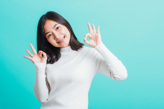 Asian teen beautiful young woman smile have dental braces on teeth laughing she showing gesturing ok sign with fingers, isolated on a blue background, Medicine and dentistry concept