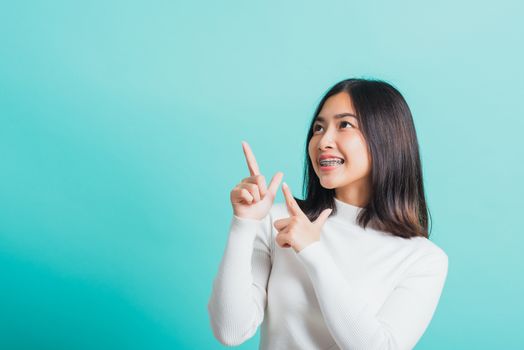 Portrait of Asian teen beautiful young woman smile have dental braces on teeth laughing point finger side away blank copy space, studio shot isolated on blue background, medicine and dentistry concept