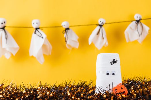 Funny Halloween day decor party concept, The mummy ghost on water glass wrapped around with bandage and have bats and spider stick it found only eyes, studio shot isolated on yellow background