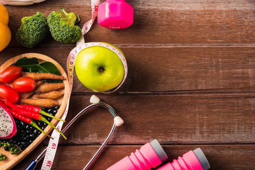 Top view of fresh organic fruit and vegetable in heart plate, shoes, sports equipment and doctor stethoscope, studio shot on wooden gym table, Healthy diet vegetarian food concept, World food day