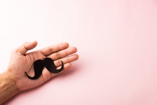 The man uses hand holding black mustache, studio shot isolated on white background, Prostate cancer awareness month, Fathers day, minimal November moustache concept