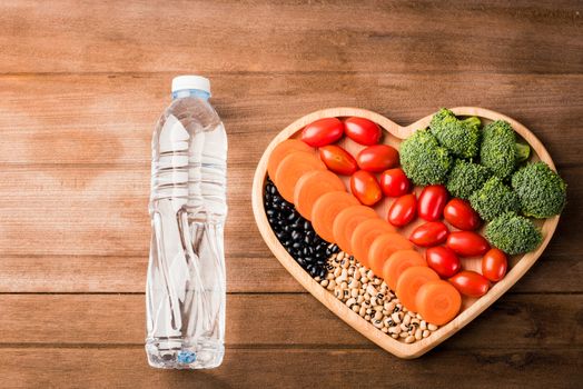 Top view of fresh organic fruits and vegetables in heart plate wood (carrot, Broccoli, tomato) and plastic water bottles on wooden table, Healthy lifestyle diet food concept