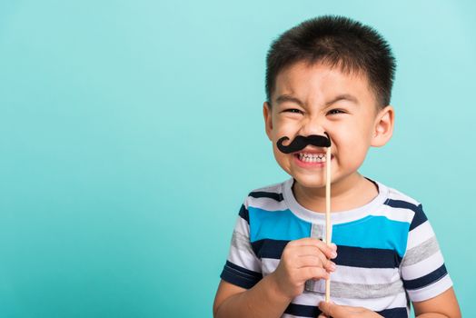 Funny happy hipster kid holding black mustache props for the photo booth close face, studio shot isolated on a blue background, Men health awareness, Prostate Cancer Awareness