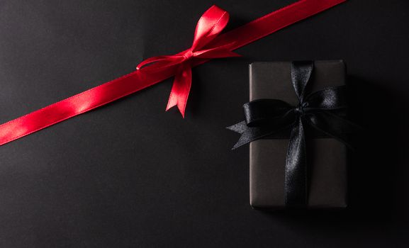 Black Friday Sale concept, Top view of gift box wrapped black paper and black bow ribbon press, studio shot on and having red ribbon across a dark background