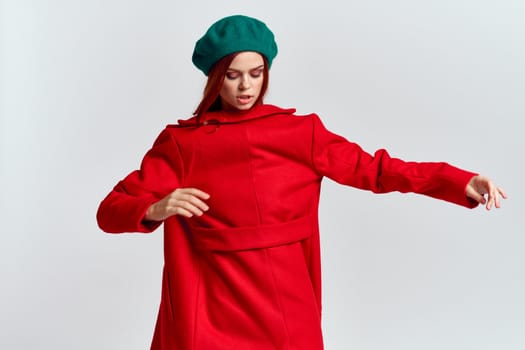 A woman holds in her hand a red coat and a dark T-shirt Green hat cropped view of a light background. High quality photo