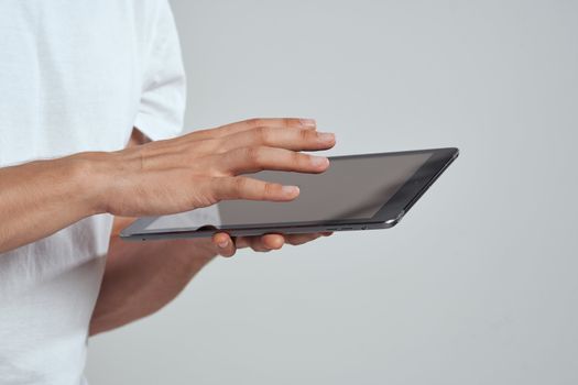 Tablet with a touch screen on a light background male hands white t-shirt cropped view. High quality photo