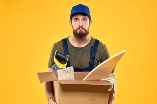 A man in a working form a box with loading tools yellow background. High quality photo