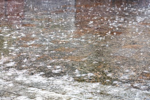 Large raindrops form an abstract pattern on the surface of the granite square of the city sidewalk. Selective focus, soft gradient of light and shadow.