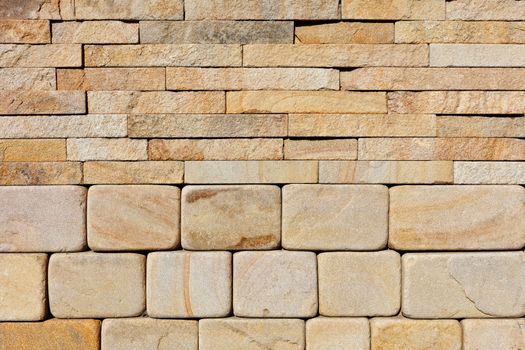 The background and texture of a wall composed of hewn rounded yellow sandstone at the base and rough rectangular tiles at the top, close-up.