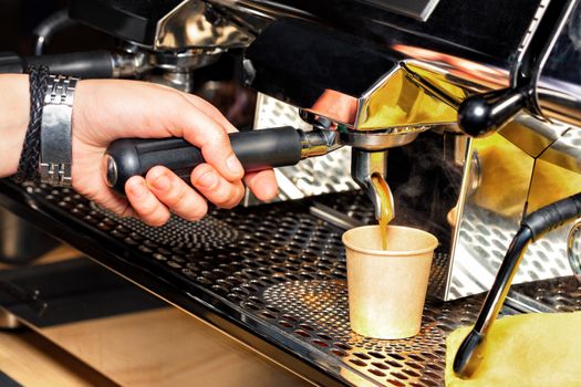 The process of making aromatic coffee, the barista holds the handle of the coffee machine in his hand and pours coffee into a cardboard cup.