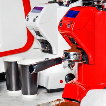 The vibrant red coffee grinder grinds the roasted beans into powder. The freshly ground coffee is scattered in the portafilter.