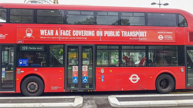 London, UK - July 8, 2020: Modern red double-decker bus is waiting for people in central London. It says on it - Wear a face covering on public transport.