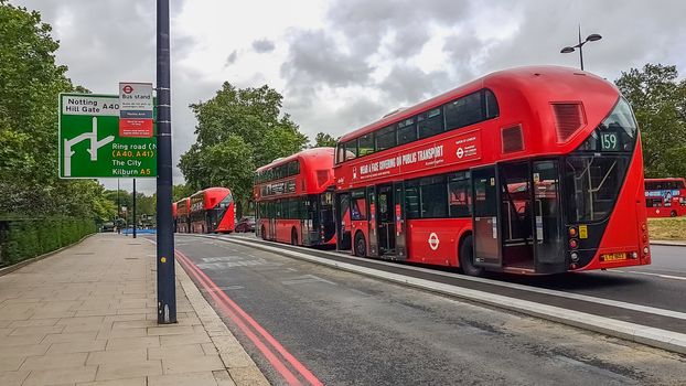 London, UK - July 8, 2020: Modern red double-decker buses waiting for people in central London by Notting Hill Gate bus stand. It says on the bus - Wear a face covering on public transport.