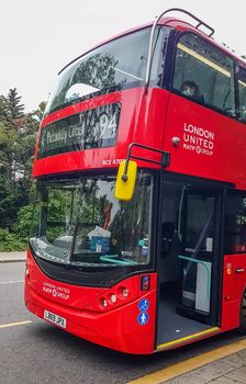 London, UK - July 8, 2020: Modern red double-decker bus is waiting for people in central London. It says on it - Piccadilly Circus 94. A person sitting on the second deck and wearing a mask.
