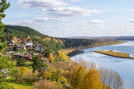 Houses along a beautiful, wide river in the middle of the forest. Calm and quiet place with autumn colors. In the middle of the river island. View from the top to the distance
