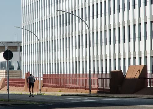 A lonely man jogs in the street early Sunday morning, in the shadow of a closed office building