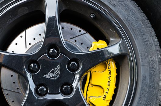 Supercar. Detail of a front tire of a Corvette. In particular the yellow brake pads, the disc and the alloy rim are highlighted