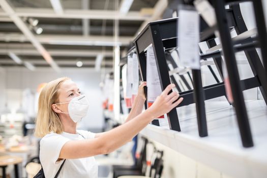 New normal during covid epidemic. Caucasian woman shopping at retail furniture and home accessories store wearing protective medical face mask to prevent spreading of corona virus.