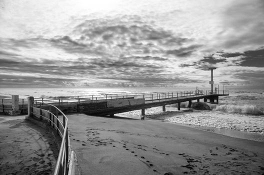 The winter sea. A jetty stretches into the waves under a cloudy skynd white