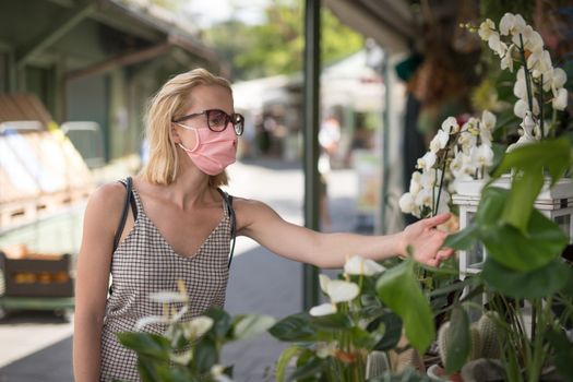 Casual woman shopping for plants outdoor at open market stalls wearing fase masks for protection from corona virus pandemic in Munchen, Germany. New normal.