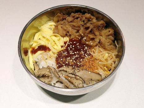 Bibimbap Korean meal consists of pork meat, egg, rice, and mushroom placed in stainless steel bowl