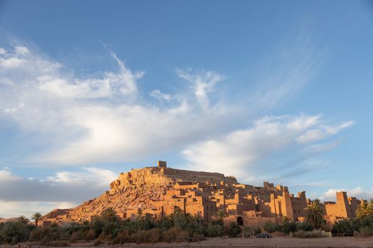 Ait Ben Haddou ksar Morocco, ancient fortress that is a Unesco Heritage site. Beautiful late afternoon light with honey, gold coloured mud brick construction against a blue sly with clouds the kasbah, or fortified town dates from 11th cent. and is on the former caravan route from the Sahara and Marrakech. The location has been used for many famous movies. High quality photo