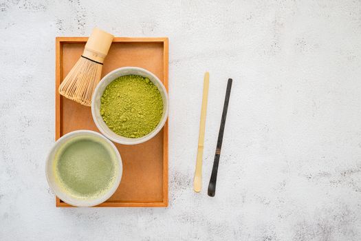 Matcha green tea powder with bamboo matcha whisk brush  setup on white concrete background .