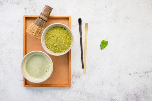 Matcha green tea powder with bamboo matcha whisk brush  setup on white concrete background .