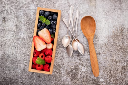 Various fresh berries blueberry, raspberry and strawberry in wooden box setup on concrete background .