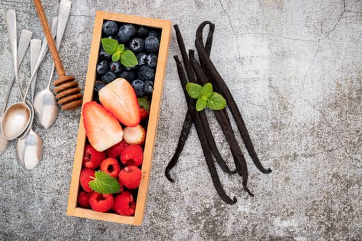 Various fresh berries blueberry, raspberry and strawberry in wooden box setup on concrete background .