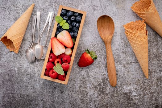 Waffle cones with berries in wooden box setup on concrete background. Summer and Sweet menu concept.