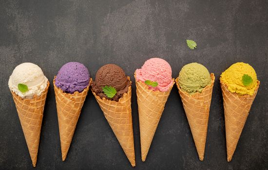 Various of ice cream flavor in cones blueberry ,pistachio ,almond ,orange and chocolate setup on dark stone background . Summer and Sweet menu concept.