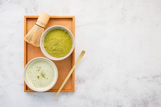 Matcha green tea powder with bamboo matcha whisk brush  setup on white concrete background .