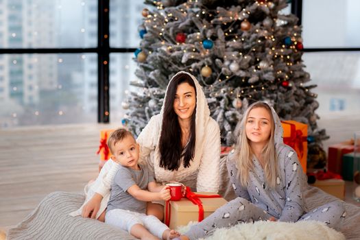 Happy cheerful family near Christmas tree. Mother and kids wearing pajama having fun near tree in the morning. Merry Christmas and Happy Holidays concept