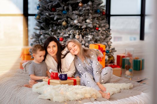 Happy cheerful family near Christmas tree. Mother and kids wearing pajama having fun near tree in the morning. Merry Christmas and Happy Holidays concept