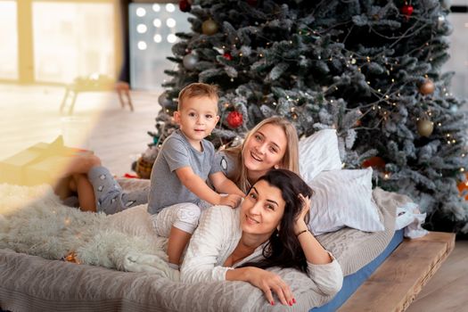 Happy cheerful family near Christmas tree. Mother and kids wearing pajama having fun near tree in the morning. Merry Christmas and Happy Holidays concept