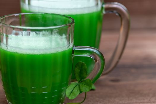 Shamrocks clovers on wooden table with a two mugs of green beer . Background for St. Patrick's Day celebration